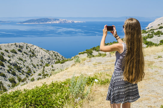 Young attractive girl taking photo of tropical landscape