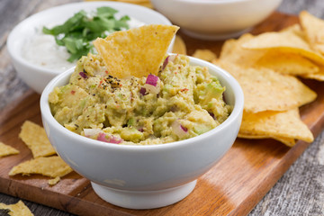 guacamole sauce, tomato salsa and corn chips on a wooden board