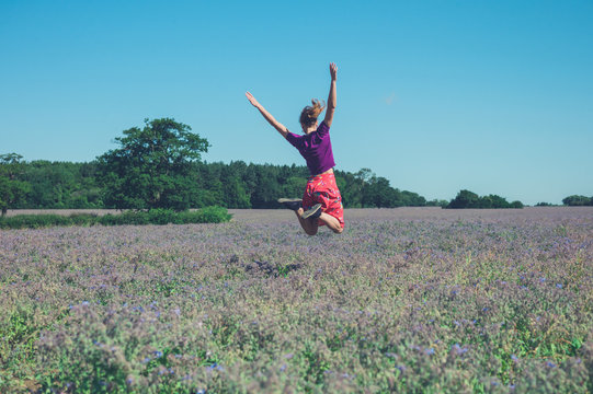 Happy young woman jumping in field of purple flowers