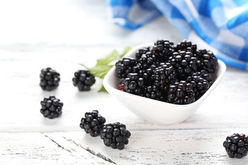 Beautiful ripe blackberry in bowl on white wooden background