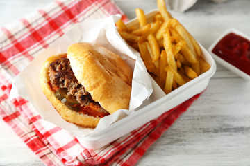 Tasty burger and french fries on plate, on wooden table background. Unhealthy food concept