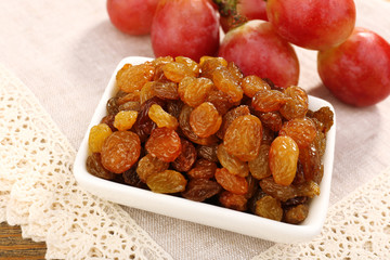 Raisins in bowl with grapes on table close up