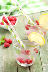 Raspberries and juice in glass on green wooden background
