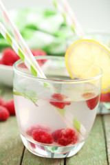 Raspberries and juice in glass on green wooden background