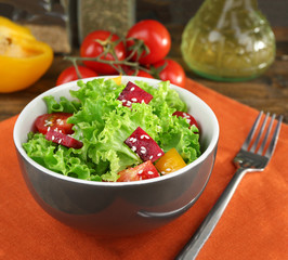 Bowl of fresh green salad on table with napkin, closeup