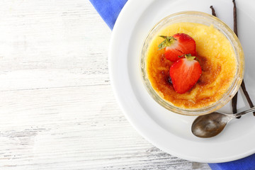 Creme brulee dessert with fresh strawberry berries on napkin, on color wooden background
