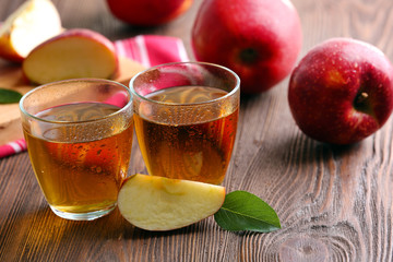 Glasses of apple juice and fruits on table close up