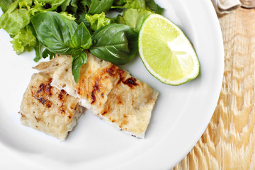 Dish of fish fillet with greens and lime on table close up