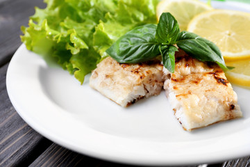 Dish of fish fillet with greens and lemon on plate close up