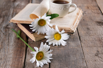 Fototapeta na wymiar Old book with beautiful flowers and cup of tea on wooden table close up