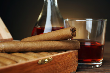 Cigars with glass of cognac on wooden table, closeup
