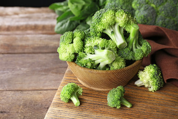 Fresh broccoli with spinach in bowl on wooden table close up