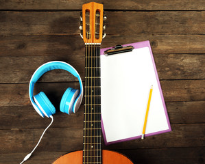 Music recording scene with classical guitar, memo pad and headphones on wooden table, closeup