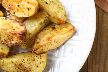 Baked spicy potatoes in white plate on wooden table, closeup