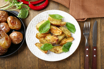 Baked potatoes with basil leaves in white plate on wooden table, top view