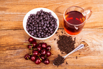 cup of tea, sweet cherry and blueberry in white bowl on a wooden