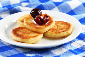 Fritters of cottage cheese with cherry and cream in plate on checkered napkin, closeup