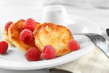 Fritters of cottage cheese with raspberries in plate on table, closeup