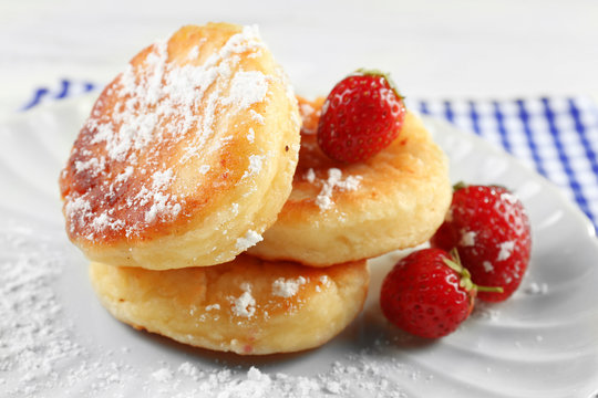 Fritters of cottage cheese with strawberry and sugar in plate on table, closeup