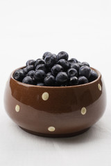 Brown dotted ceramic bowl filled with bilberries, rustic style. Wooden table  striped blue white towel background, homely. Vertical.