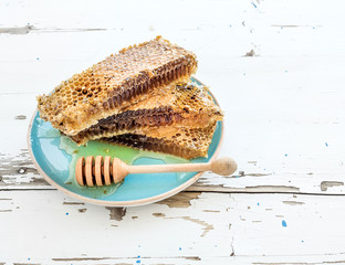 Honeycomb with honey dipper on blue ceramic plate over rustic