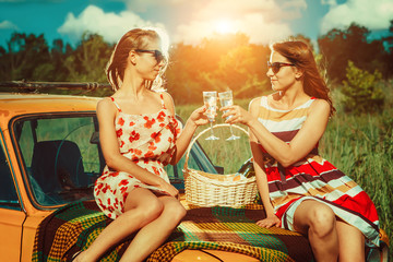 Two beautiful women on the picnic are drinking champagne on the