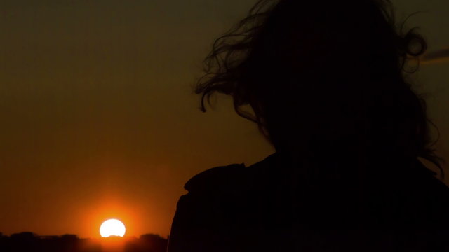 Dark silhouette of woman looking at sunset, wind waving her hair. Changes