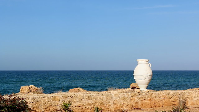 Simple background illustrating Greece.Amphora reminds rich culture,history of country,clear sky turquoise sea - beautiful holiday weather,yellow brown stone wall and specific plants - tropical weather