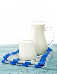 Pitcher and glass of milk on wooden table, on white background