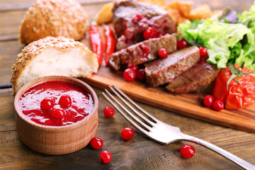 Beef with cranberry sauce, roasted potato slices on cutting board, on wooden background