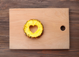 Pineapple slice with cut in shape of heart on wooden background