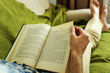 Young man reading book on sofa close up