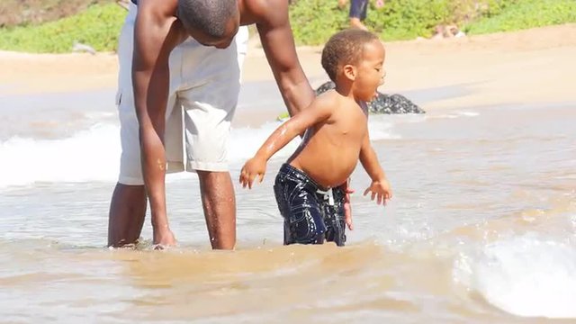 Black toddler playing in the ocean with his father