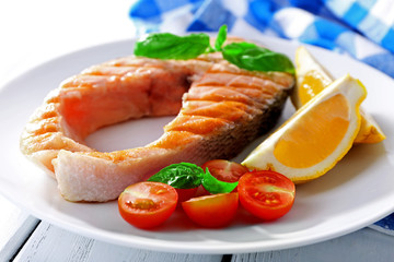 Tasty grilled salmon with tomato and lemon on table close up