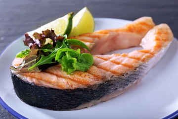 Tasty grilled salmon with greens on table close up