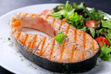 Tasty grilled salmon with salad on table close up