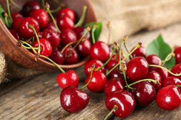 Fresh cherries in bowl on wooden table with sackcloth, closeup