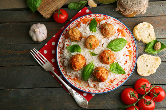 Meat balls in tomato sauce with boiled rice and lentil, wooden spoon on wooden background