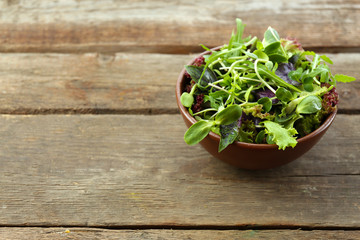 Fresh mixed green salad in bowl on wooden table close up