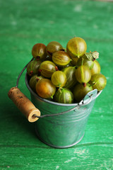 Green gooseberry in pail on wooden background