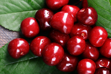 Sweet cherries with green leaves on wooden background