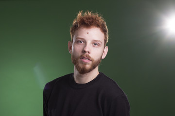 Portrait of ginger beautiful male model, laying in green grass.