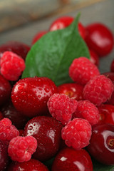 Sweet cherries, raspberries with green leaves on wooden background