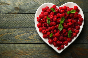 Sweet raspberries on plate, on wooden  background