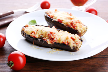 Dish of eggplant with cherry tomatoes and cheese in white plate on wooden table, closeup