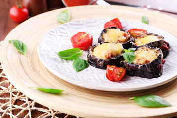 Dish of eggplant with cherry tomatoes and cheese in white plate on wooden table, closeup