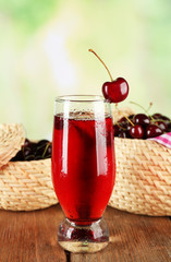 Glass of cherry juice on wooden table on light blurred background