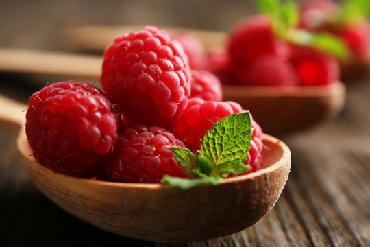 Fresh red raspberries in spoons on wooden table, closeup