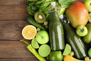Green healthy juice with fruits and vegetables on wooden table close up