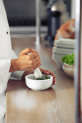Cook hands with mortar with herbs on bright background